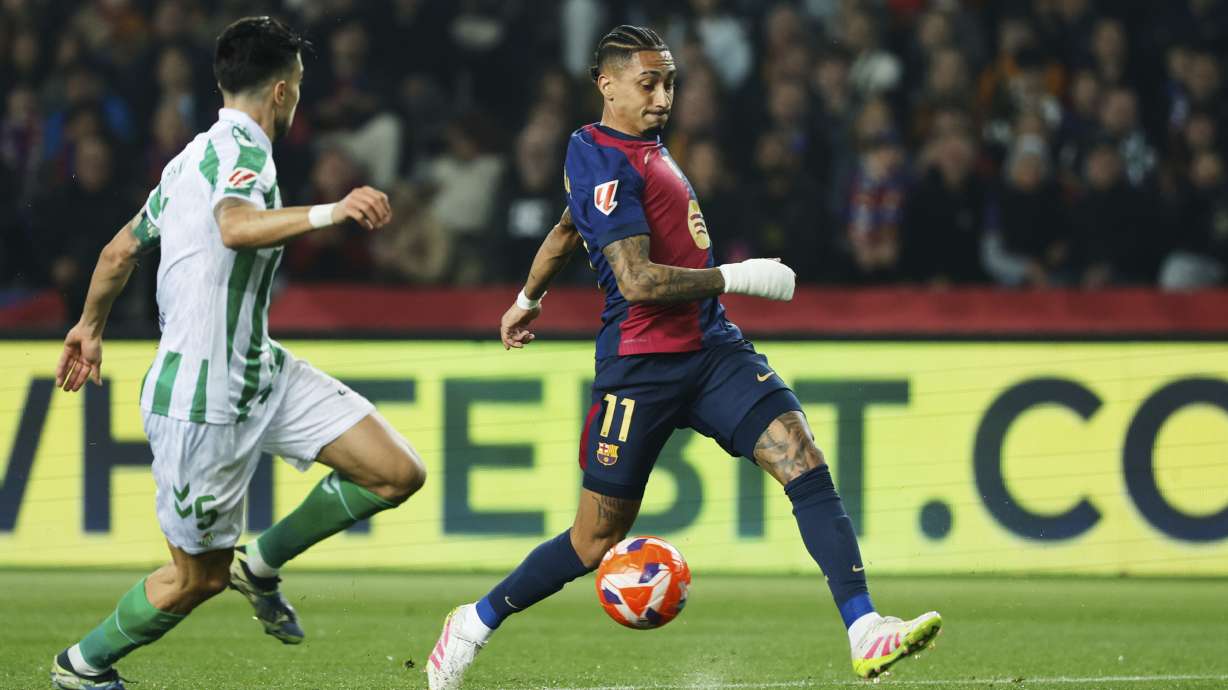 Barcelona's Raphinha, right, dribbles the ball past Betis' Marc Bertra during a Spanish La Liga soccer match between Barcelona and Real Betis at the Lluis Companys Olympic stadium in Barcelona, Spain, Saturday, April 5, 2025.