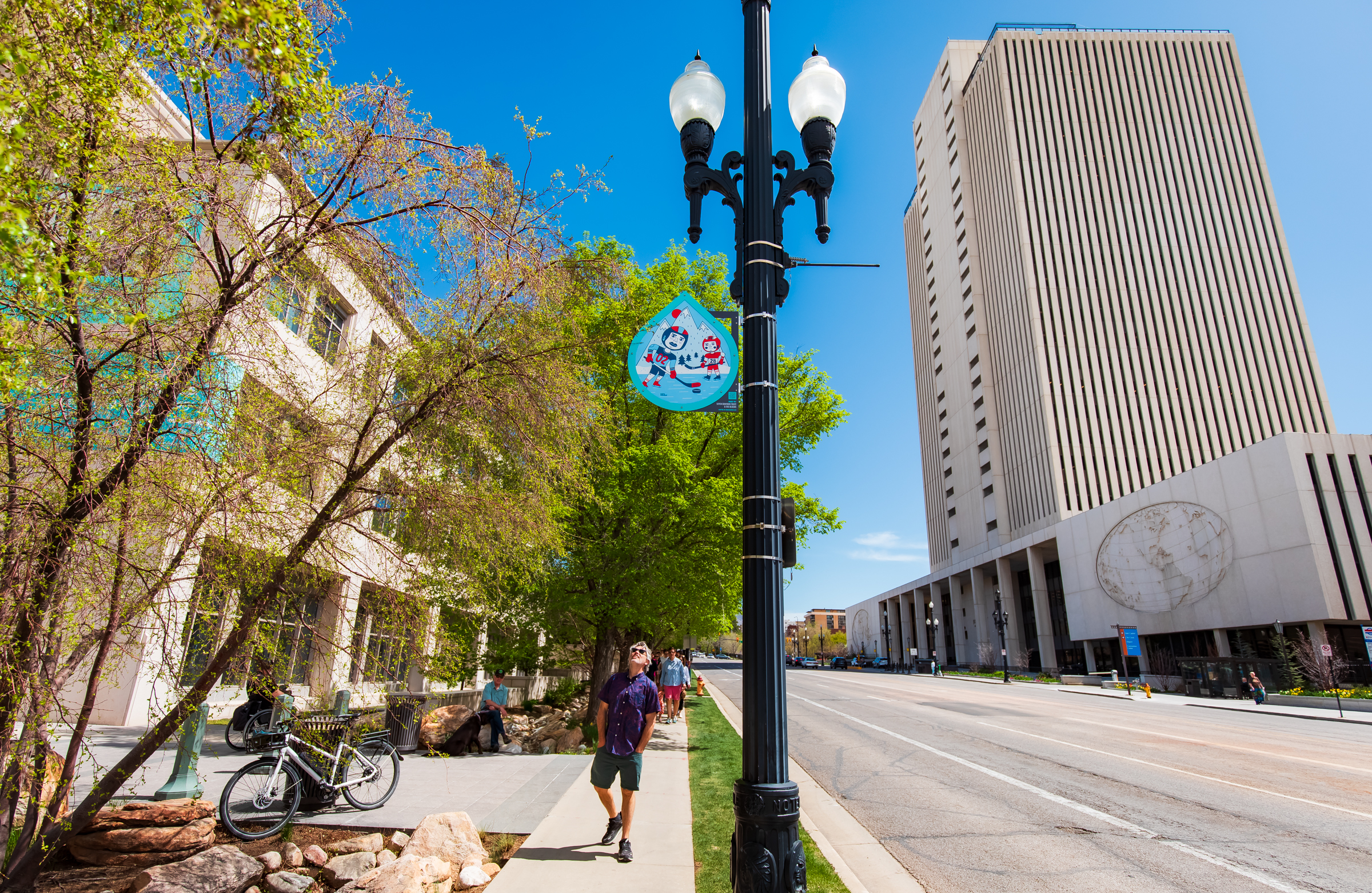 A person looks up to view an art piece designed by Kate Wolsey, depicting the importance of water and Olympic sports, hanging atop a light pole along North Temple in Salt Lake City on Friday.
