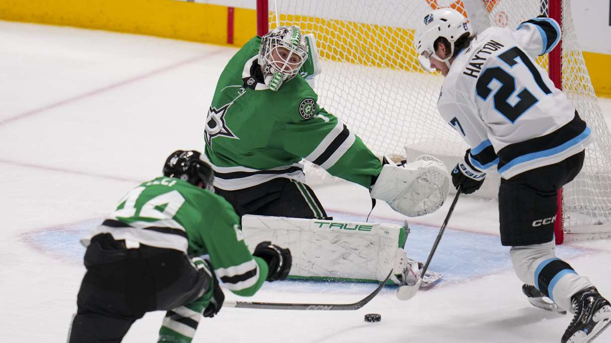 Utah Hockey Club center Barrett Hayton (27) attacks against Dallas Stars goaltender Casey DeSmith (1) and defenseman Cody Ceci (44) during the third period of an NHL hockey game Saturday, April 12, 2025, in Dallas.