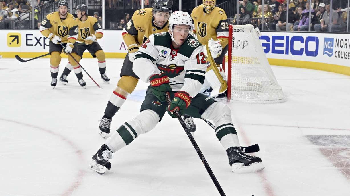 Minnesota Wild left wing Matt Boldy (12) and Vegas Golden Knights defenseman Nicolas Hague (14) battle for the puck during the first period of Game 2 of a first-round NHL hockey playoff series Tuesday, April 22, 2025, in Las Vegas.