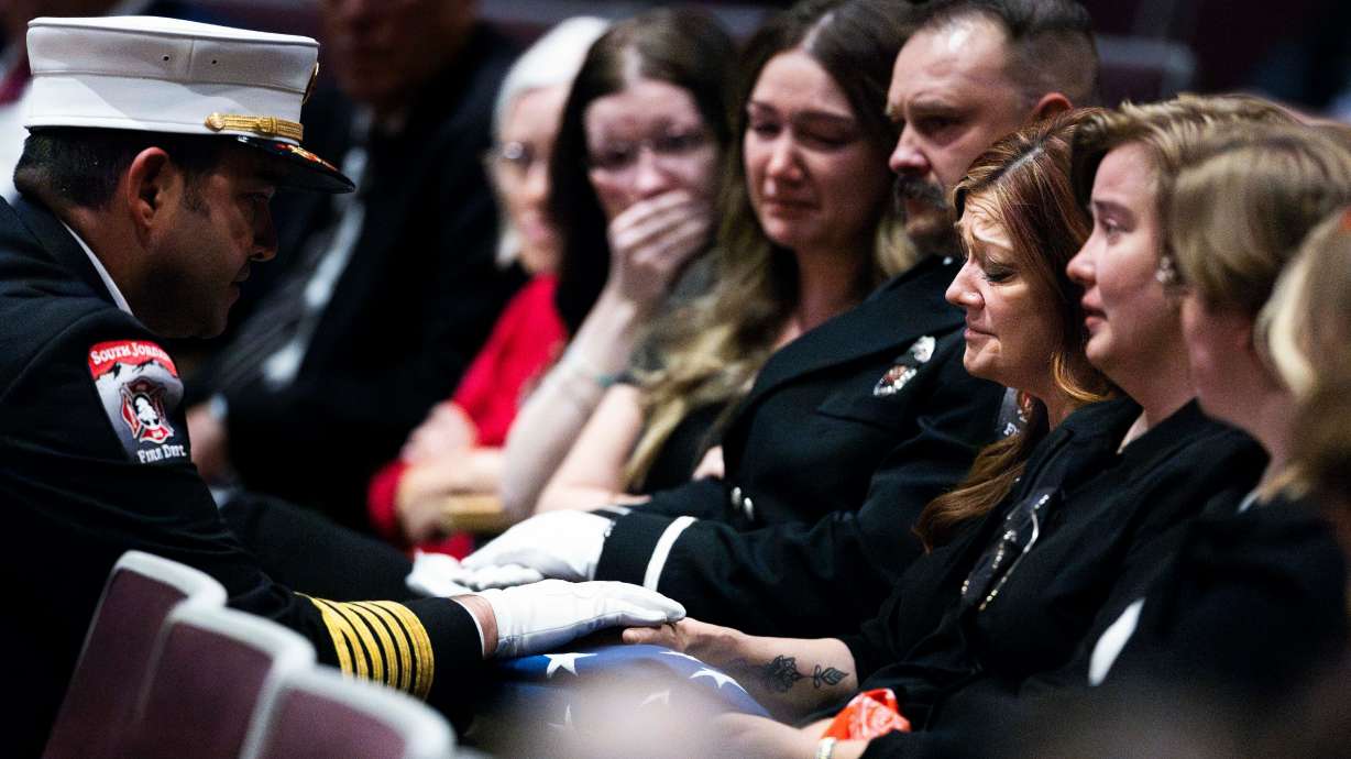 A firefighter presents the flag from the casket to Kim Summers, the wife of the late South Jordan firefighter Corban Summers, during a funeral service for Corban Summers at Hunter High School in West Valley City on Saturday.