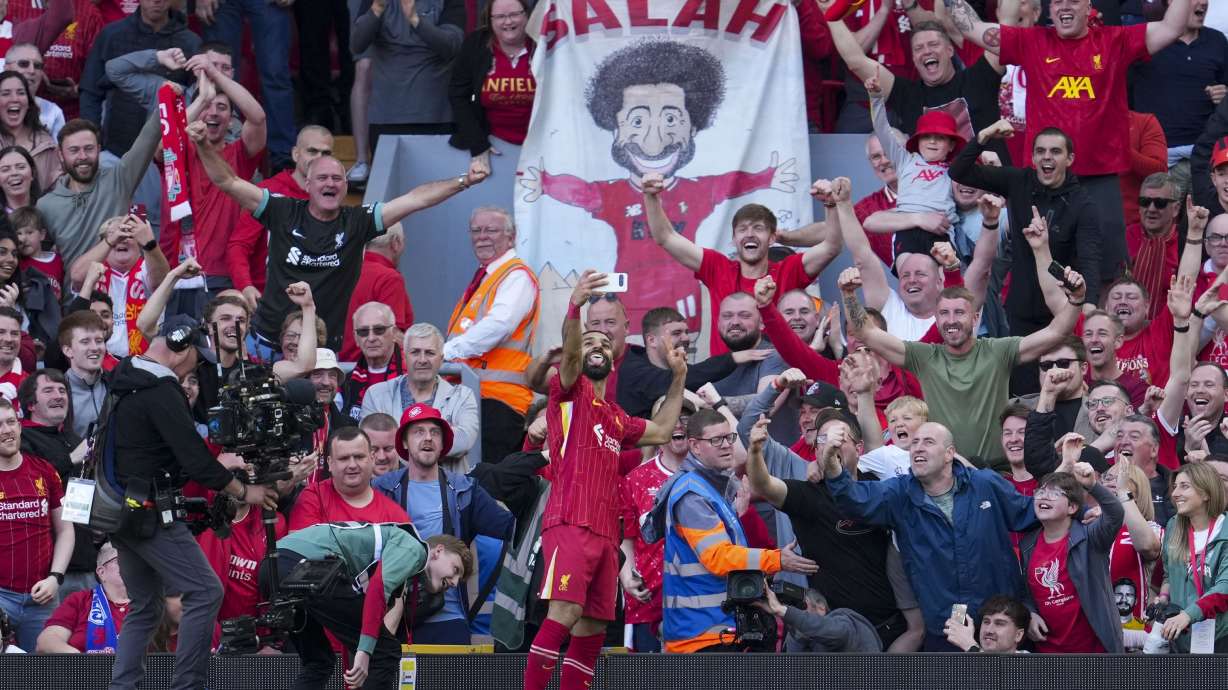 Liverpool's Mohamed Salah takes a selfie with a fans smartphone as he celebrates after scoring his side's fourth goal during the English Premier League soccer match between Liverpool and Tottenham Hotspur at Anfield in Liverpool, England, Sunday, April 27, 2025.