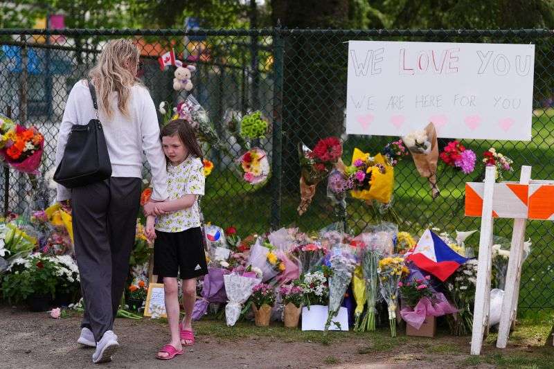 Visitors stand near a growing memorial the day after a driver killed multiple people during a Filipino community festival Sunday, in Vancouver, Canada.