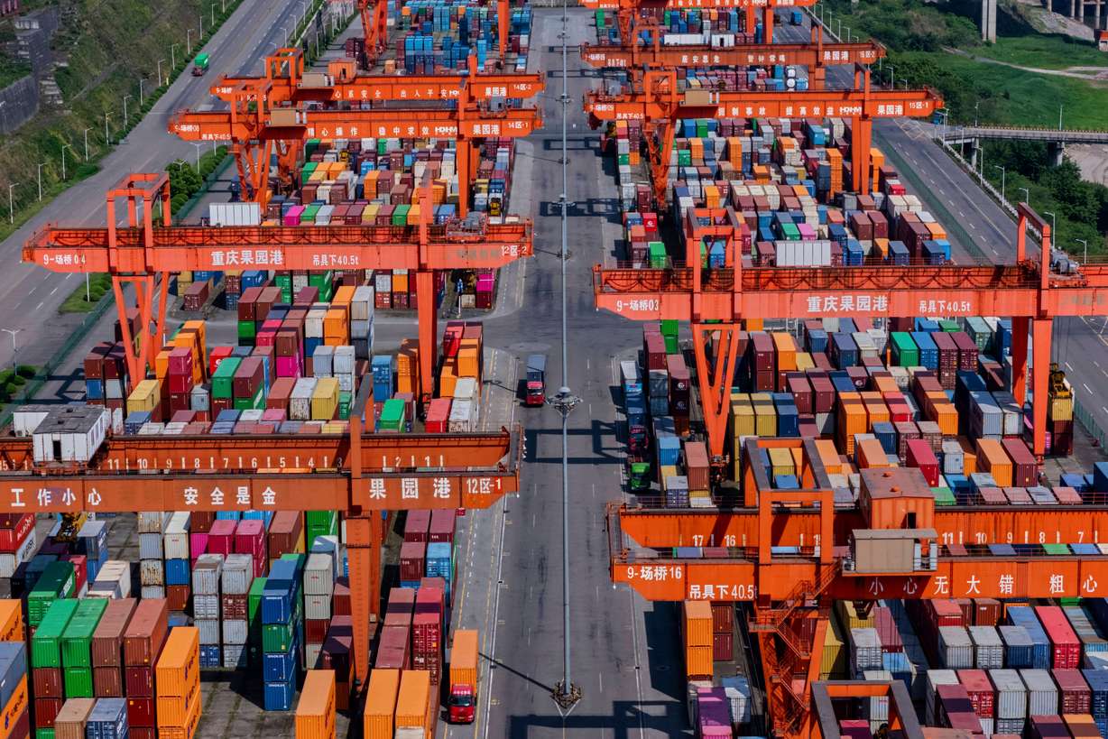 Trucks move past piles of containers stacked at a container terminal port on the Yangtze River in southwest China's Chongqing Municipality on April 20.