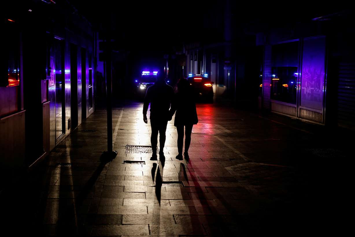 People walk along a shopping street without electric lighting as police cars patrol to prevent theft and looting in the stores during a power outage which hit large parts of Spain, in Ronda, Spain Monday.
