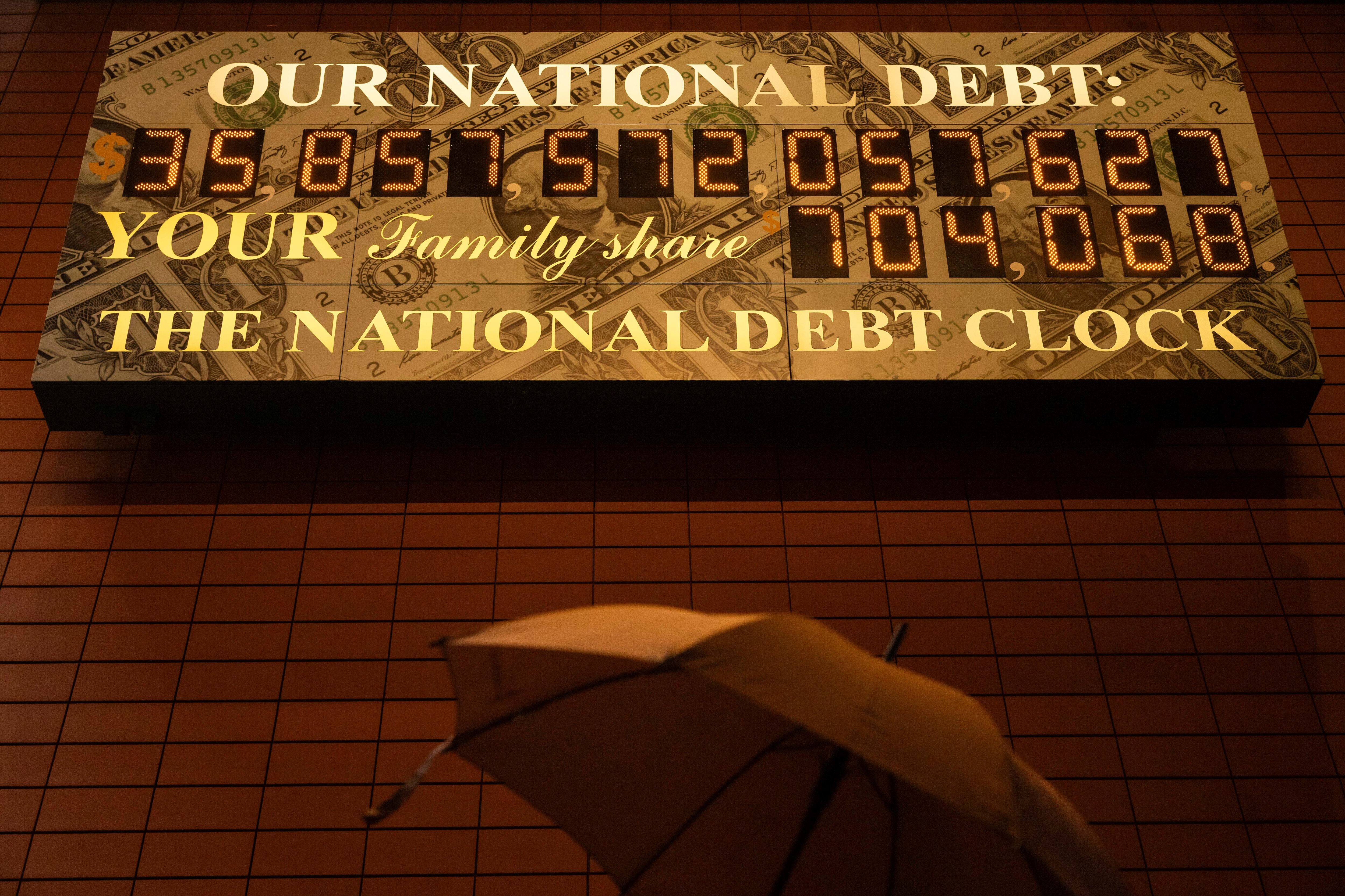 A person carrying an umbrella walks past the National Debt Clock, April 7 in New York.