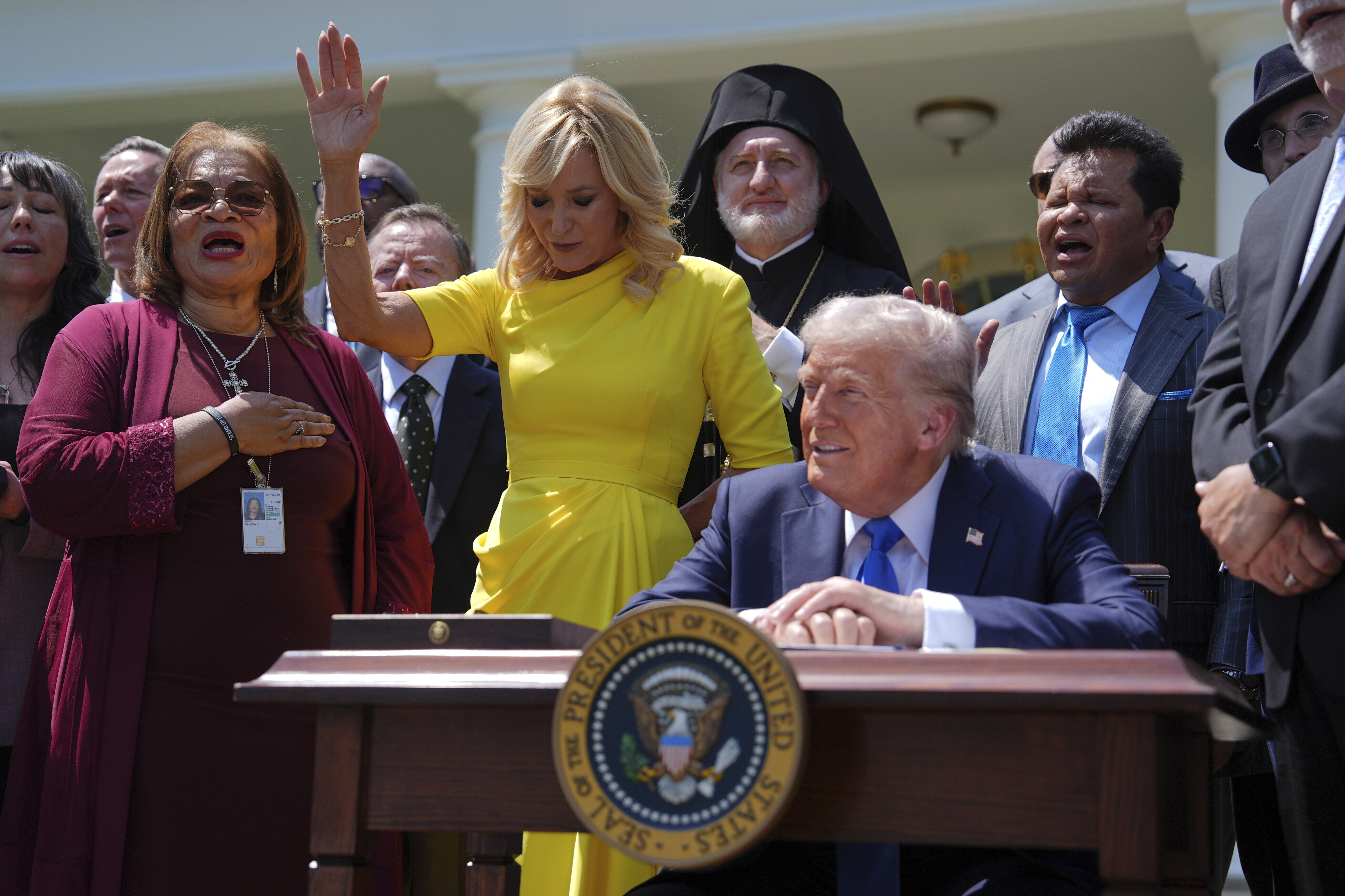 President Donald Trump sits at a desk as he and religious leaders listen to a musical performance before Trump signs an executive order during a National Day of Prayer event in the Rose Garden of the White House, Thursday, in Washington.