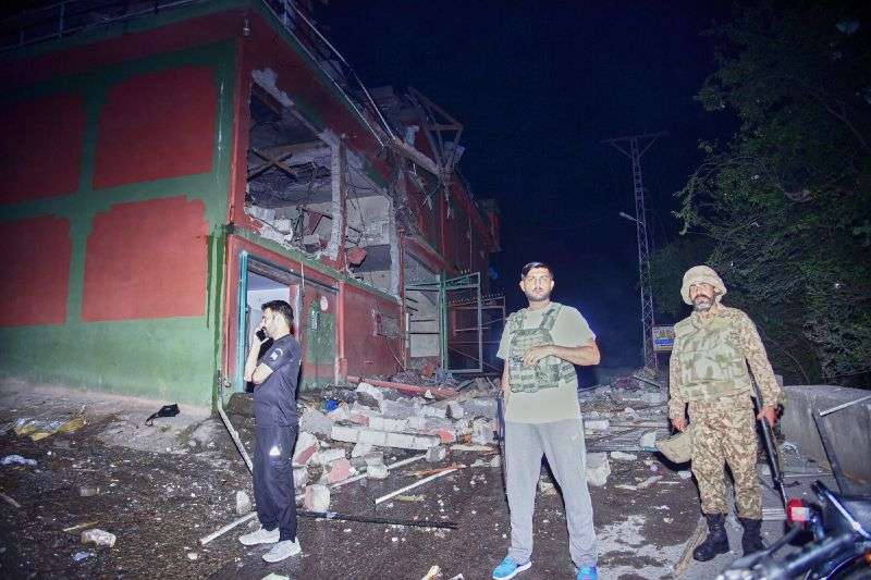Security force officials stand outside a damaged building at a site of a suspected Indian missile attack near Muzaffarabad, the capital of Pakistan controlled Kashmir, in Wednesday