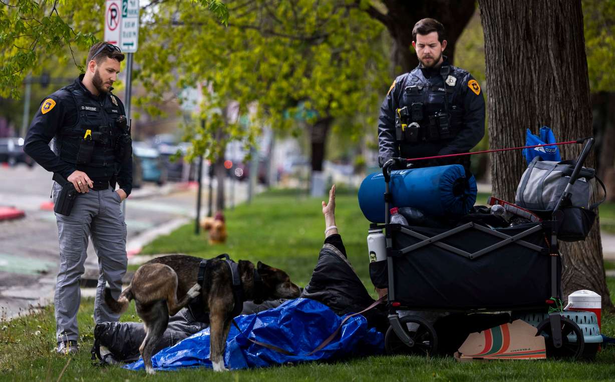 Salt Lake City police detective Dalton Beebe, left, and Salt Lake City police officer Michael Donahoo, right, inform a homeless man that he can’t sleep on the grass along the sidewalk in Salt Lake City on April 17.