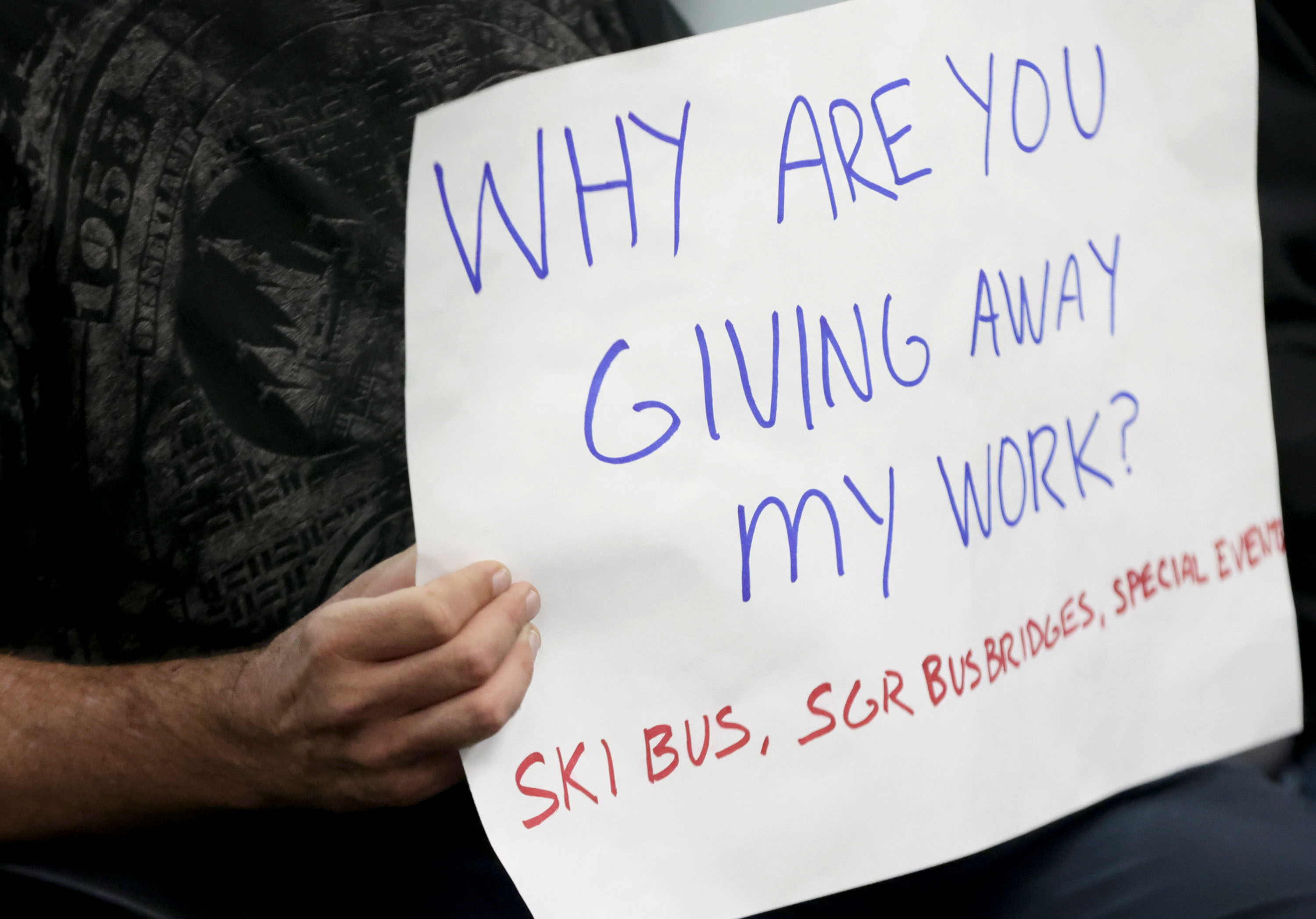 Bryant Barker, a Utah Transit Authority bus driver for the past year, holds a sign while speaking to board members during a UTA board meeting in Salt Lake City on Wednesday.