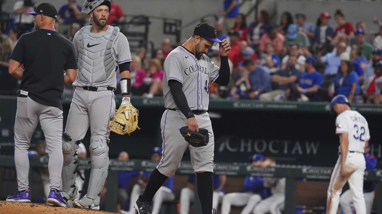 Colorado Rockies starting pitcher Antonio Senzatela, right, leaves play as interim manager Warren Schaeffer, left, and catcher Jacob Stallings stand on the mound during the fifth inning of a baseball game against the Texas Rangers, Wednesday, May 14, 2025, in Arlington, Texas.