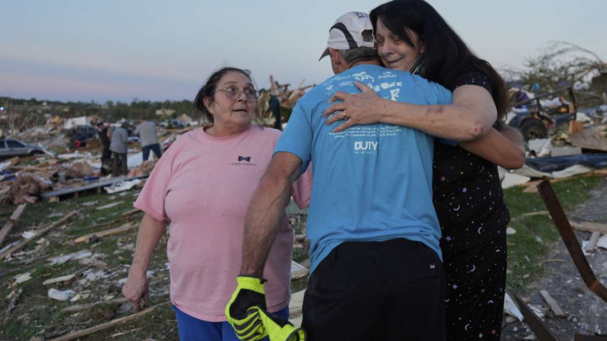 Bea Johnson, left, looks to her sister Kristie Sexton, right, as she is embraced by family friend Keith Adams as they stand next to Sexton's destroyed home after a severe storm passed through the area, Saturday, in London, Ky.