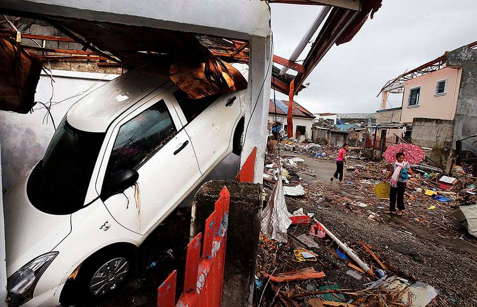 A car is upended in its parking stall as people walk the debris-strewn streets in Tacloban, Nov. 22, 2013, following Typhoon Haiyan in the Philippines.