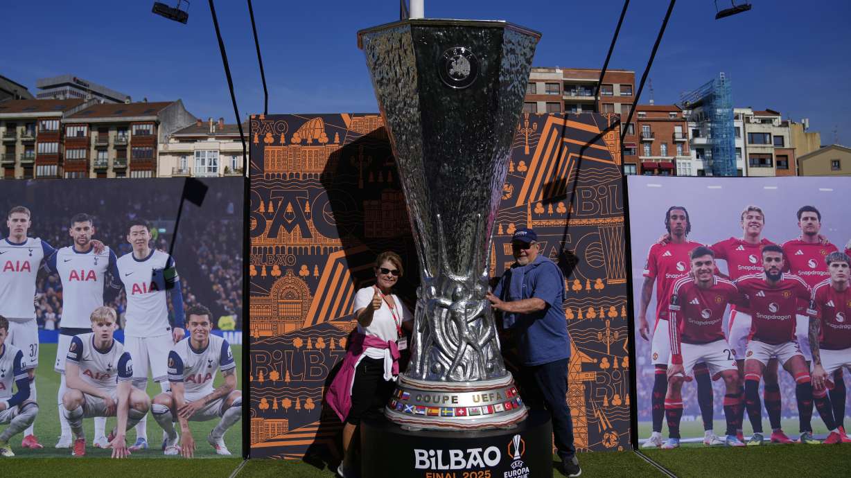 Fans pose for a photo next to a giant replica of the Europa League trophy ahead of the final soccer match between Tottenham Hotspur and Manchester United at the San Mamés Stadium in Bilbao, Spain, Wednesday, May 21, 2025.