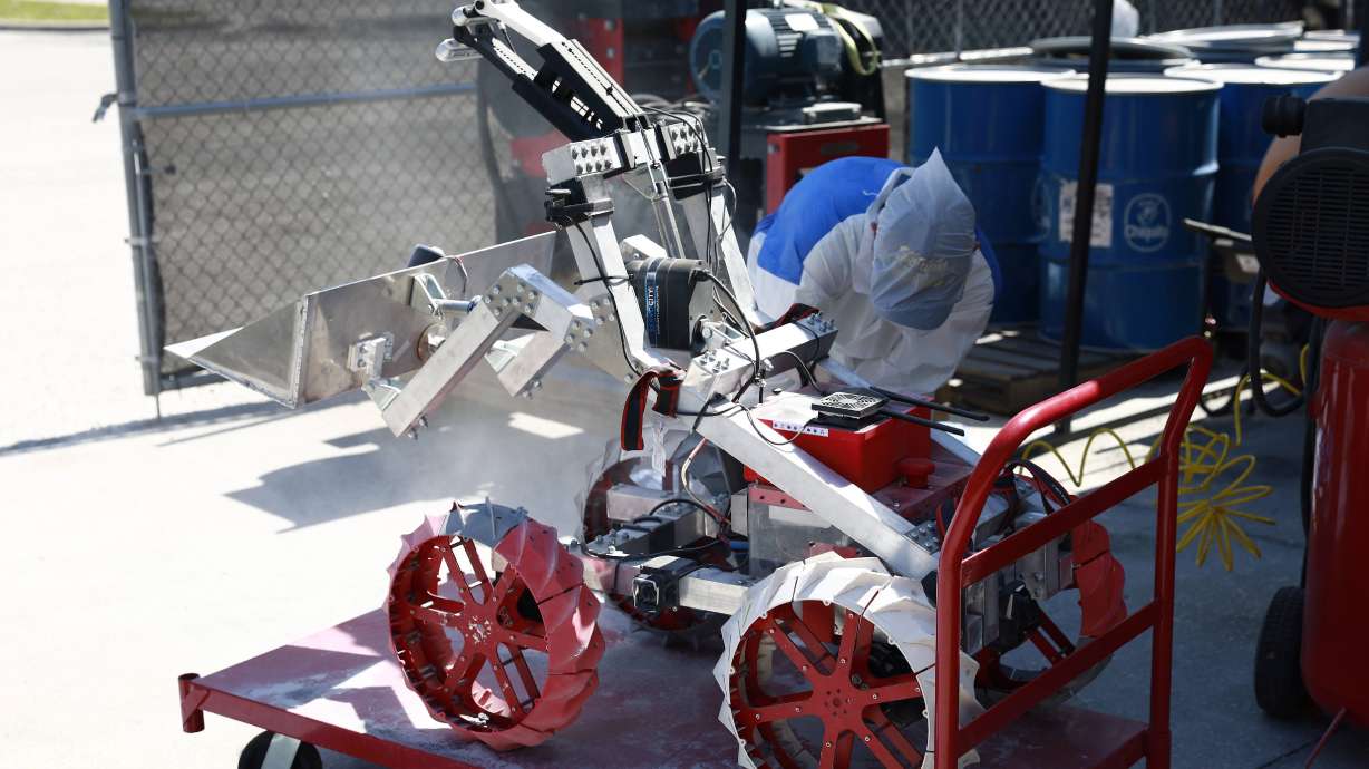 Students wearing personal protective equipment clean simulated lunar dust off a team robot. Utah Student Robotics participated in the NASA Lunabotics Challenge and won several awards, including the grand prize.