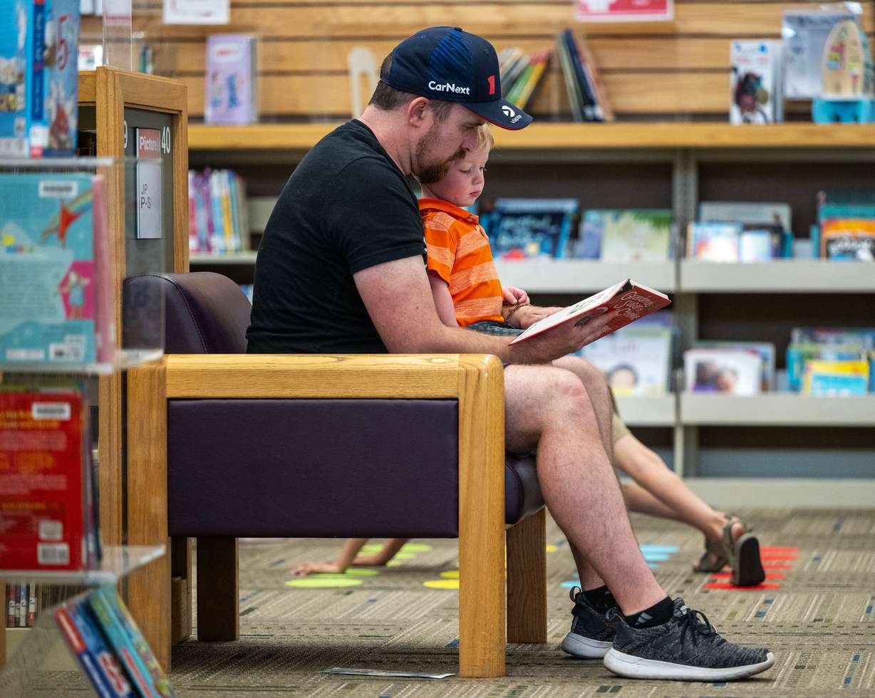 Kevin Despain reads to his son Adam Despain as Taylorsville Library holds its summer reading kickoff party on May 30.