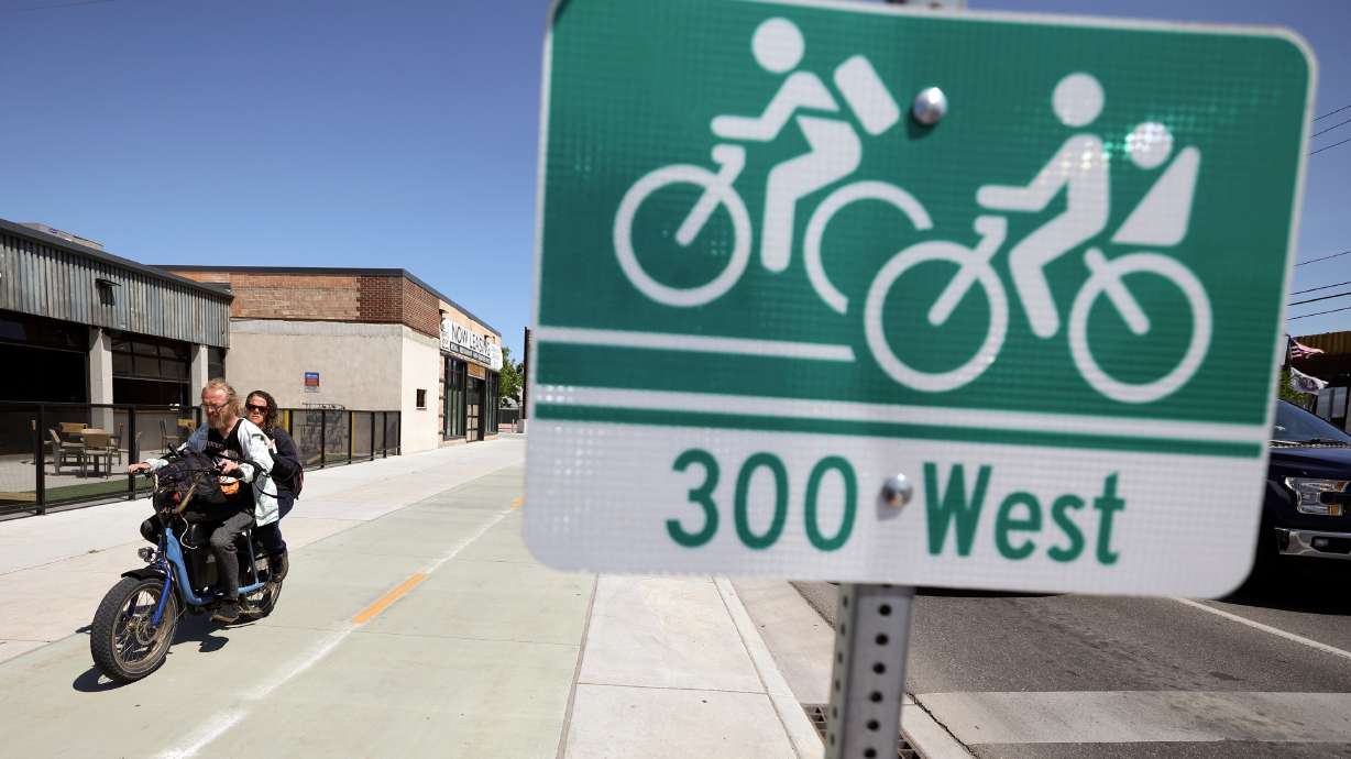 Jared Grinnell and Teresa Martinez ride an e-bike on the 300 West bikeway in Salt Lake City June 3, 2025. A proposed new bill released Tuesday calls on the city to partner with state transportation officials before enacting any new traffic safety measures.