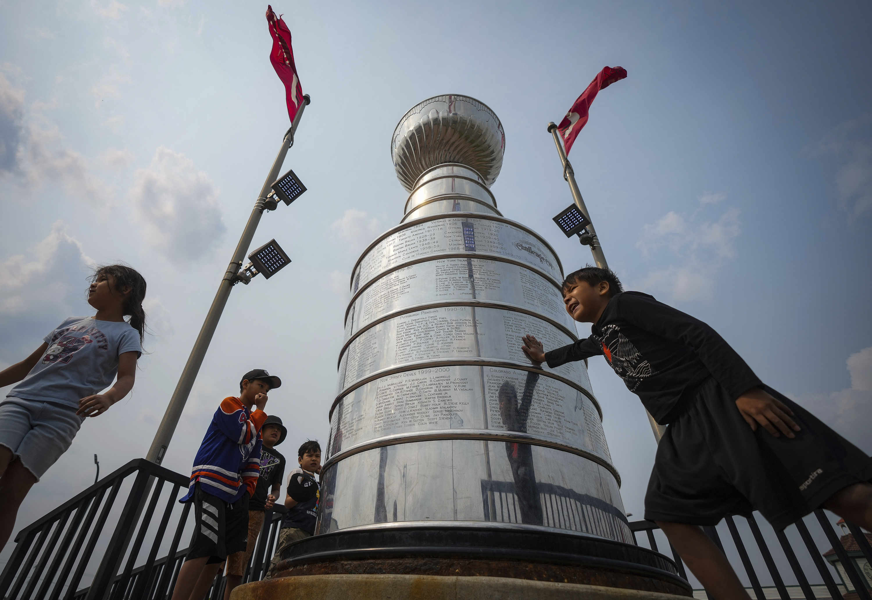 Kids from Pierceland, Saskatchewan, in the city on vacation, stop to touch and look at a nearly 4 meter replica of the Stanley Cup trophy, Tuesday, June 3, 2025, that is a permanent installation in Edmonton, Alberta, ahead of Game 1 of the NHL hockey Stanley Cup final series between the Florida Panthers the Edmonton Oilers.