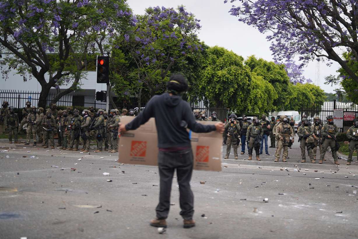 A protester holds a sign in front of Border Patrol personnel in Paramount, California, Saturday. The Trump administration deployed 2,000 National Guardsmen in response to continued clashes between federal agents and protestors of immigration raids.