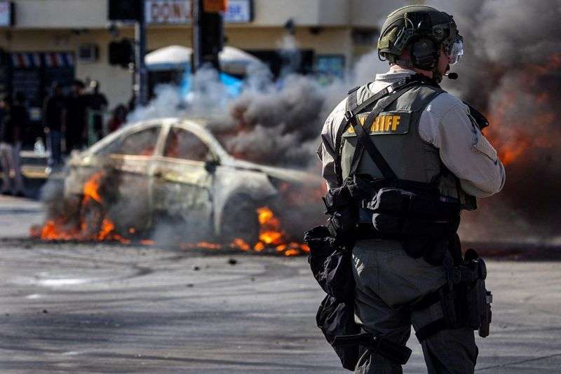 Smoke rises from a burning car on Atlantic Boulevard, during a standoff by protesters and law enforcement, following multiple detentions by Immigration and Customs Enforcement, in the Los Angeles County city of Compton, Calif., on Saturday.