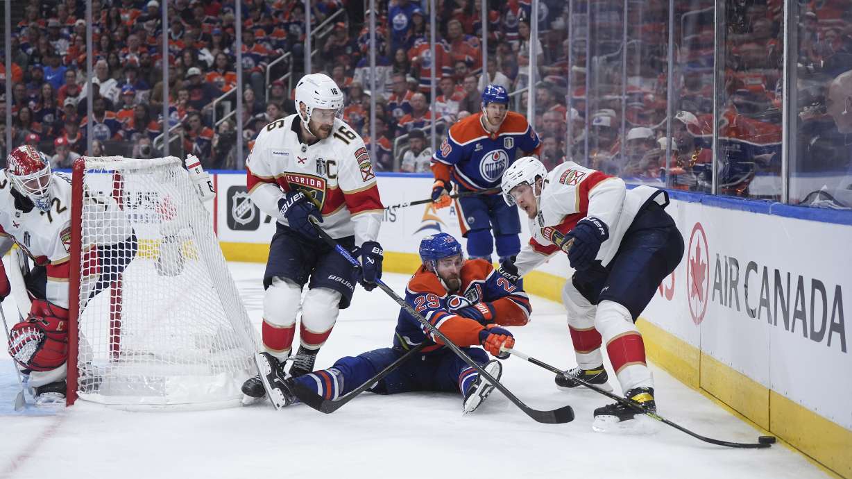 Edmonton Oilers' Leon Draisaitl, center, reaches for the puck after being checked to the ice behind Florida Panthers goalie Sergei Bobrovsky (72) as Aleksander Barkov (16) and Evan Rodrigues (17) defend during the first overtime period in Game 2 of the NHL Stanley Cup Final, in Edmonton, Alberta, Friday, June 6, 2025.