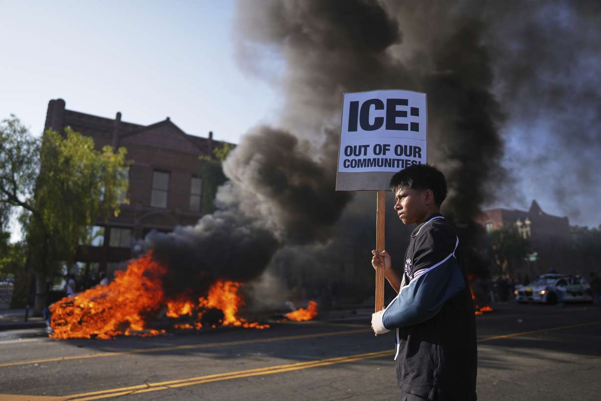 A protester holds a sign as a Waymo taxi burns near the Metropolitan Detention Center of downtown Los Angeles on Sunday.