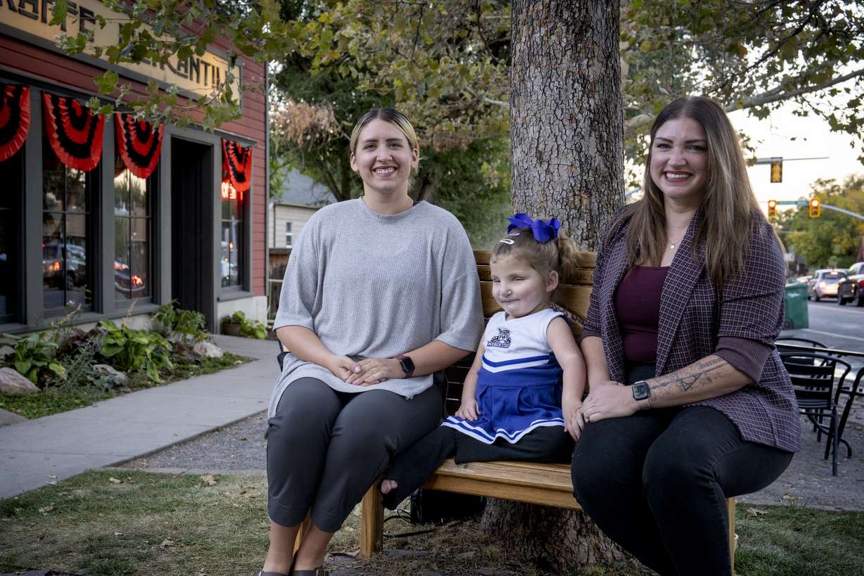 Kari and Kassie Harbath, along with Kari's daughter Sloan, sit on a bench dedicated to their mother outside Kaffe Mercantile in Ogden on Oct. 2, 2024. The sisters created a scholarship fund for their late mother who loved Weber State University.
