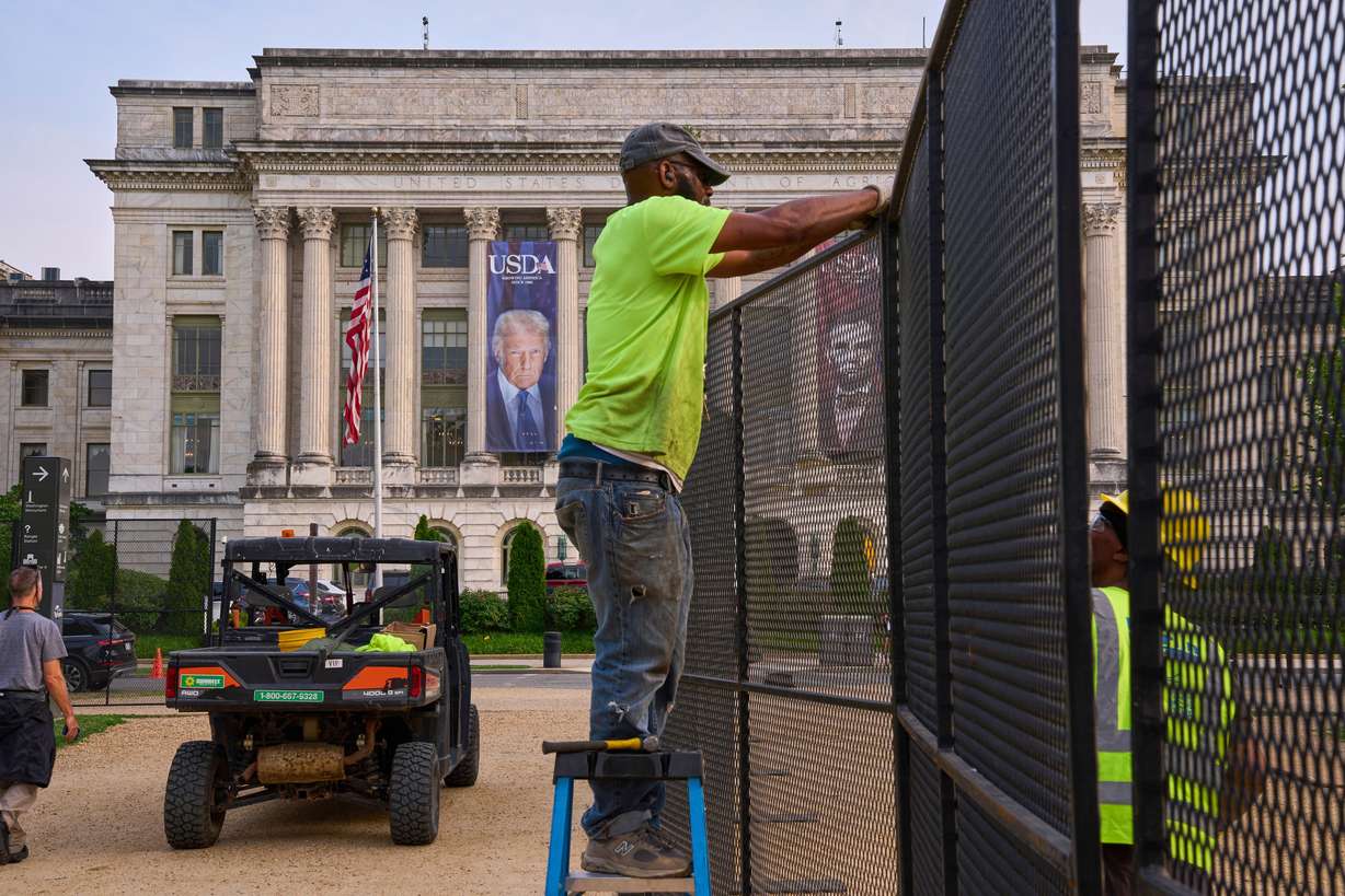 Workers install security fencing on the National Mall, Tuesday, outside the USDA Whitten Building, where a large photograph of President Donald Trump is draped, in Washington.