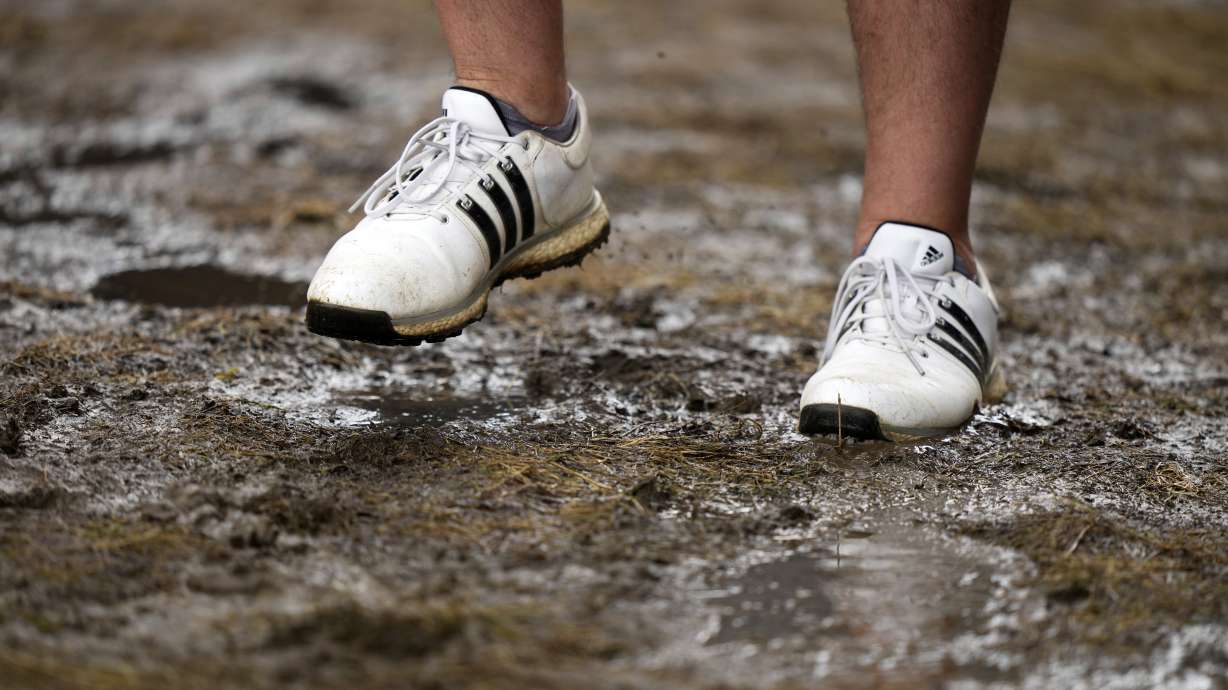 A fan walks through a soggy puddle near the 14th hole during the third round of the U.S. Open golf tournament at Oakmont Country Club Saturday, June 14, 2025, in Oakmont, Pa.