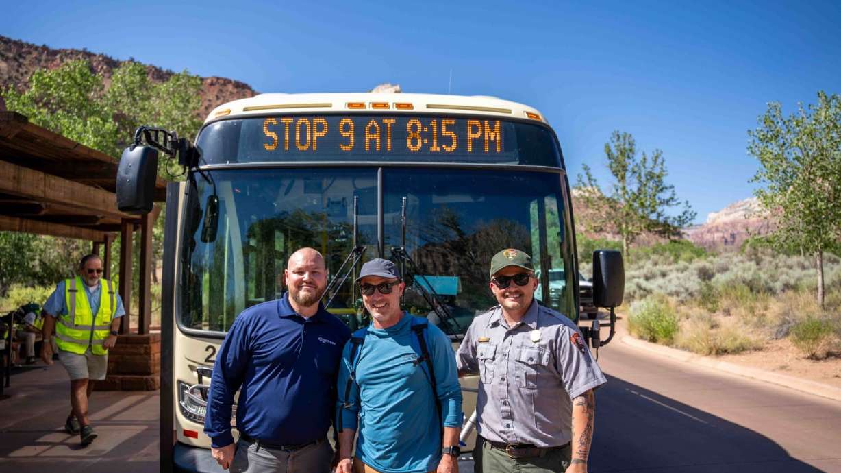 Alex Wiest, center, is celebrated as the Zion Canyon Shuttle System's 100 millionth rider by a representative from RATPDev, the shuttle bus concessioner, left, and a park ranger.