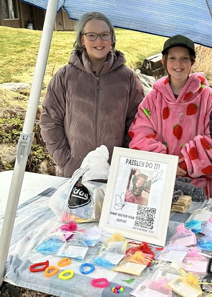 Bay and Kenzie Killam stand by a stand where they are raising money for Paisley Knapp, a young girl fighting neuroblastoma.
