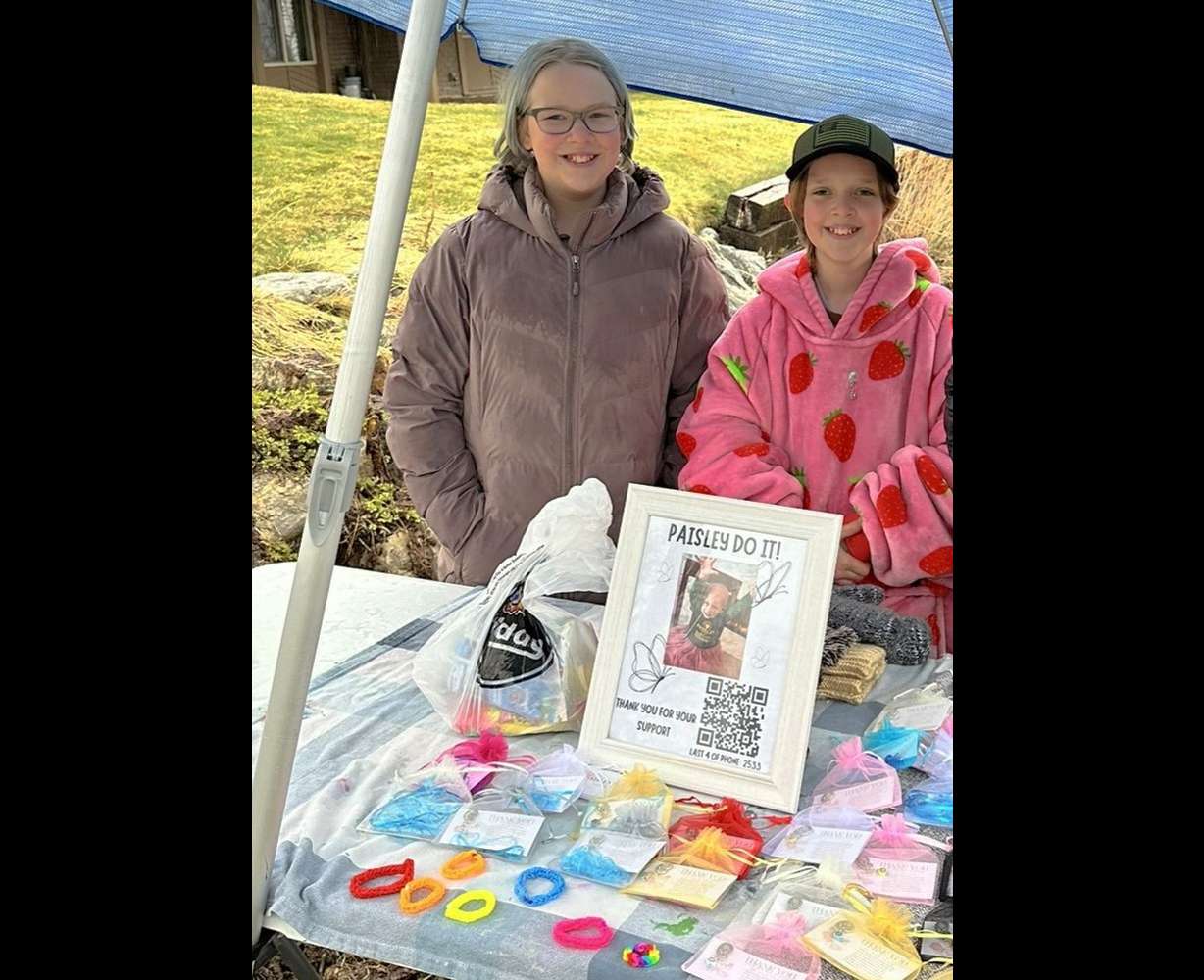 Bay and Kenzie Killam stand by a stand where they are raising money for Paisley Knapp, a young girl fighting neuroblastoma.