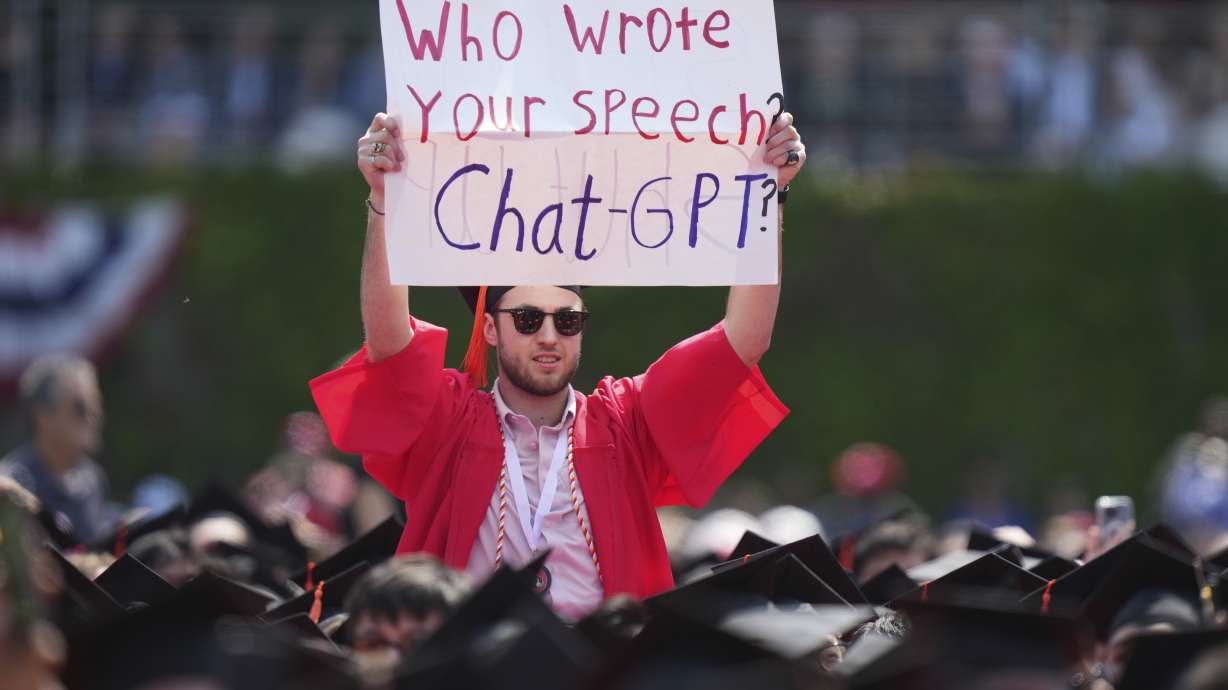 A person in a graduation cap and gown holds a sign during an address by David Zaslav, president and CEO of Warner Bros. Discovery, at Boston University commencement ceremonies, May 21, 2023, in Boston.