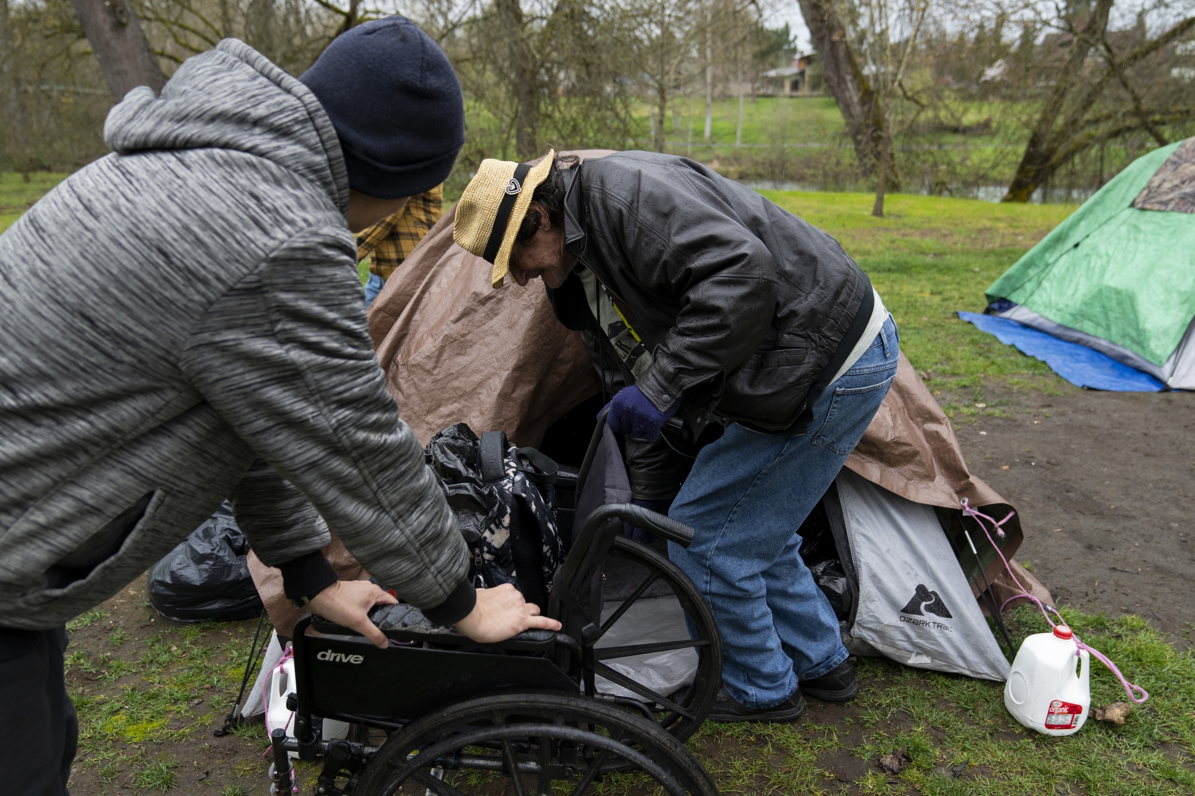 A volunteer holds on to a wheelchair as they help Max Hartfelt into his tent after relocating him from one park to another on March 23, 2024, in Grants Pass, Ore.