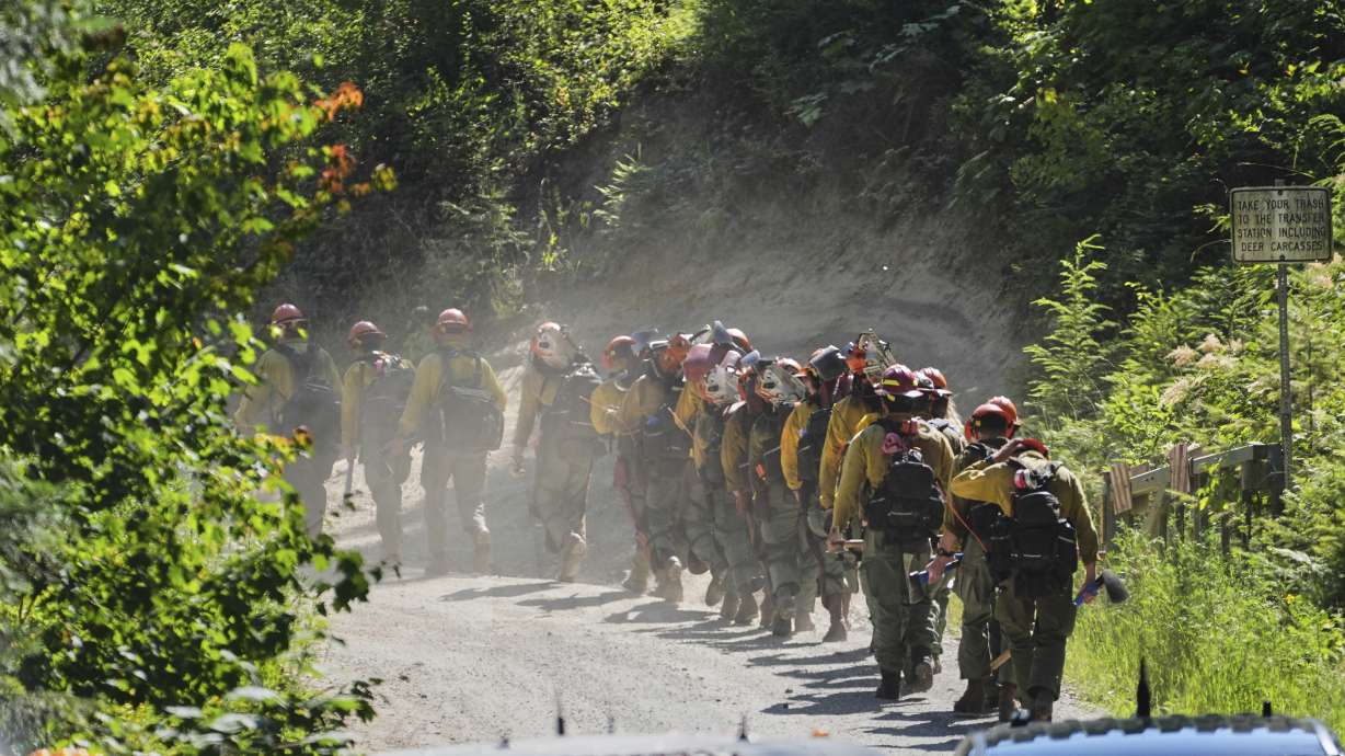 A line of wildland firefighters arrive at the scene the day after a shooter ambushed and killed multiple firefighters responding to a wildfire Monday, in Coeur D'Alene, Idaho.
