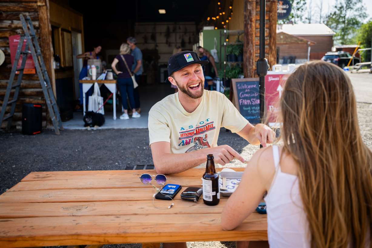 Konrad Collins, center, laughs with friend Ellery Ross, right, as they eat food made by SmokeWood, a mobile food trailer, at Gracie's Farm in Wanship on Friday, June 20, 2025.