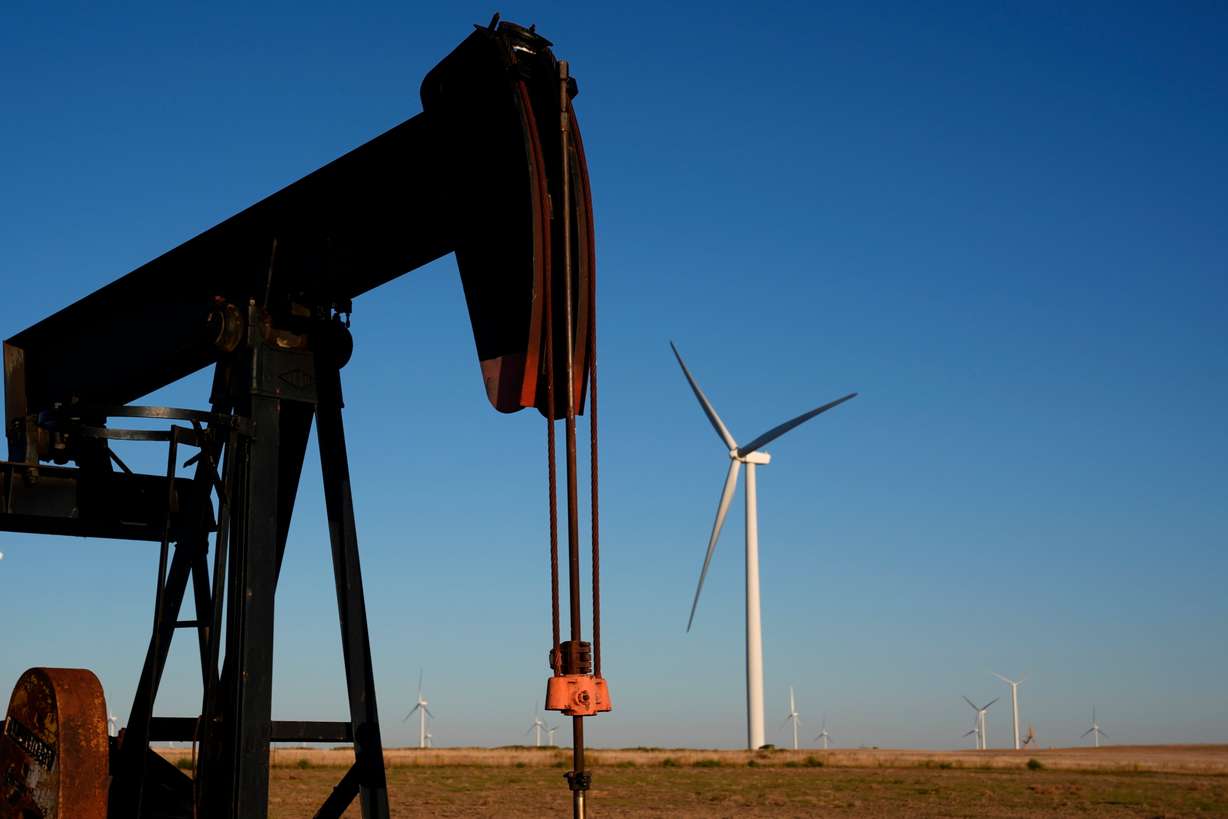 Pumpjacks operate in the foreground while wind turbines at the Buckeye Wind Energy wind farm rise in the distance, Sept. 30, 2024, near Hays, Kan.