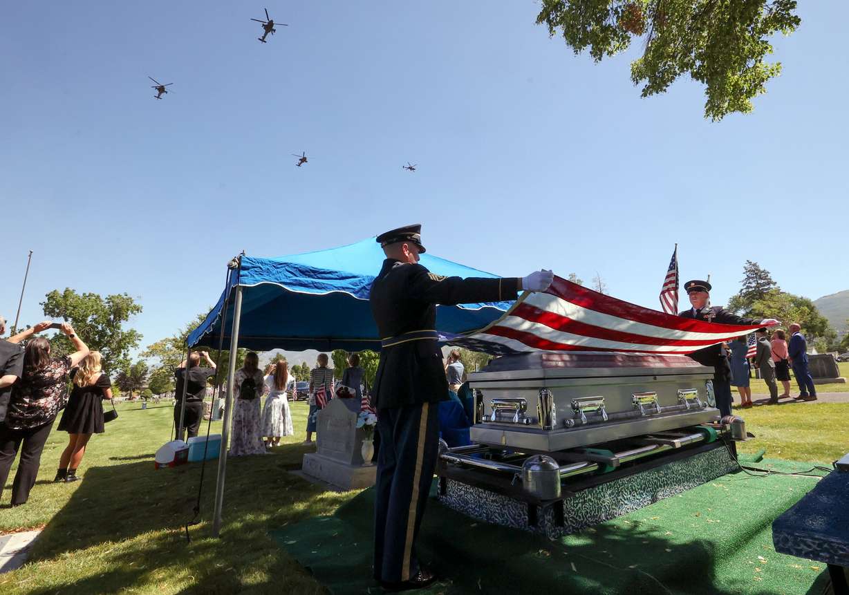 1st Sgt. Cory Bybee and Staff Sgt. Dakota Dejong hold a flag over the casket of 1st Lt. George Wilson as four Apache attack helicopters fly overhead at Bountiful City Cemetery on Tuesday. Wilson's remains arrived in Utah only a few days ago.