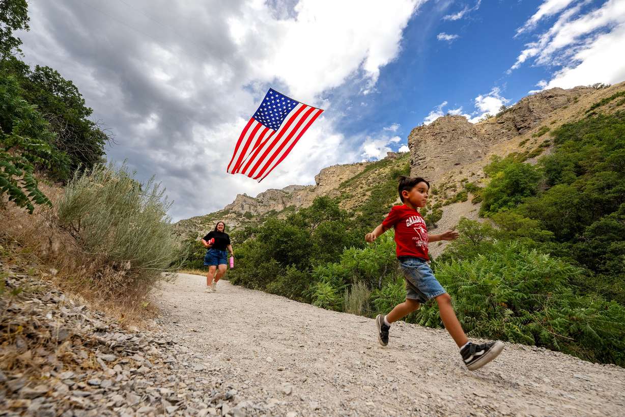 Alexis Daw and her son, Milo Meza, run down a trail under the "Follow The Flag" flag as it waves in the wind in Grove Creek Canyon, Pleasant Grove, on Wednesday. Kyle Fox flies "the world's biggest American flag" every summer at Grove Creek Park in his hometown of Pleasant Grove.