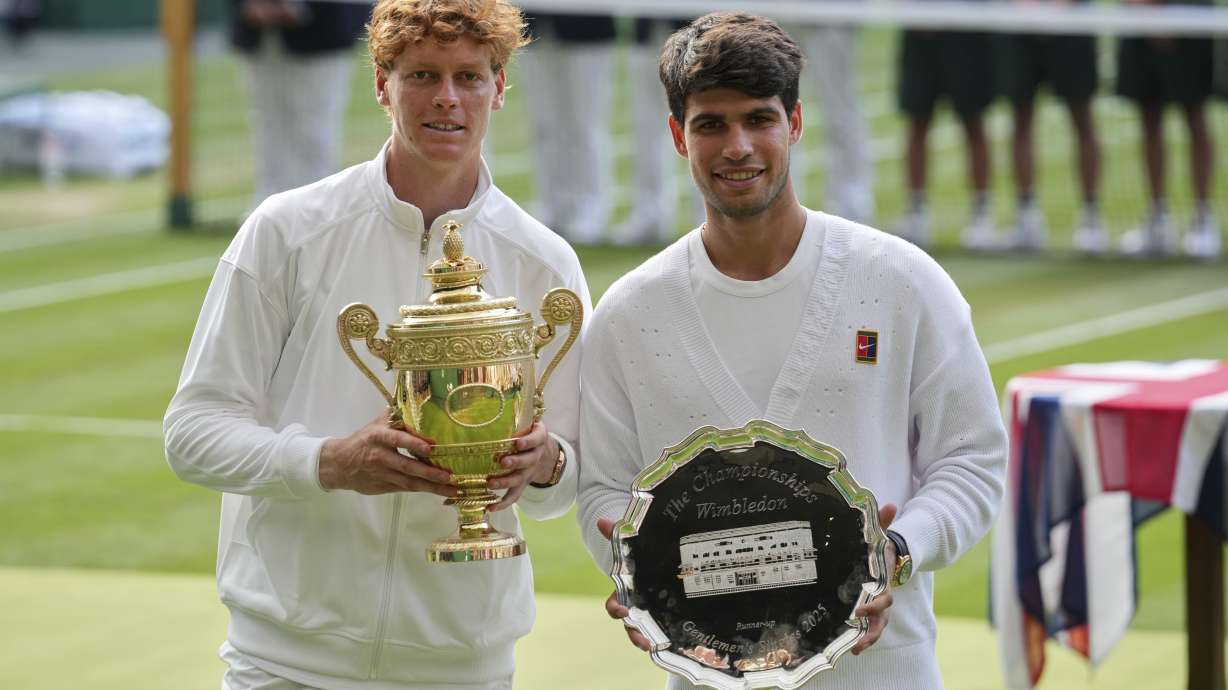 Italy's Jannik Sinner, left, celebrates with the trophy after beating Carlos Alcaraz of Spain, right, to win the men's singles final at the Wimbledon Tennis Championships in London, Sunday, July 13, 2025.