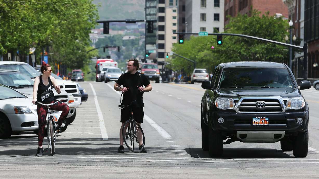 Bicyclists wait for a light in the bike lane, June 1, 2015, in Salt Lake City. Cyclists frequently encounter vehicles parked in the bike lane, forcing them into traffic and creating a dangerous situation for them and for drivers.