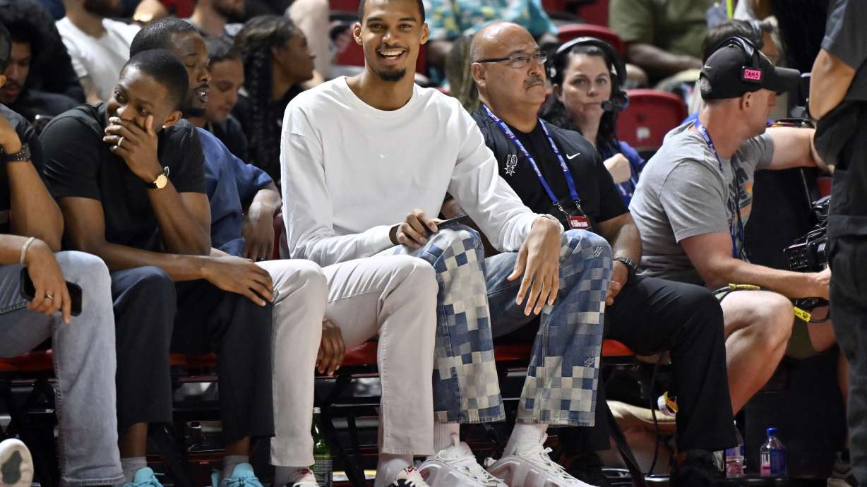 San Antonio Spurs' Victor Wembanyama, center, sits court side during the first half of an NBA summer league basketball game between the Spurs and Philadelphia 76ers, Thursday, July 10, 2025, in Las Vegas.