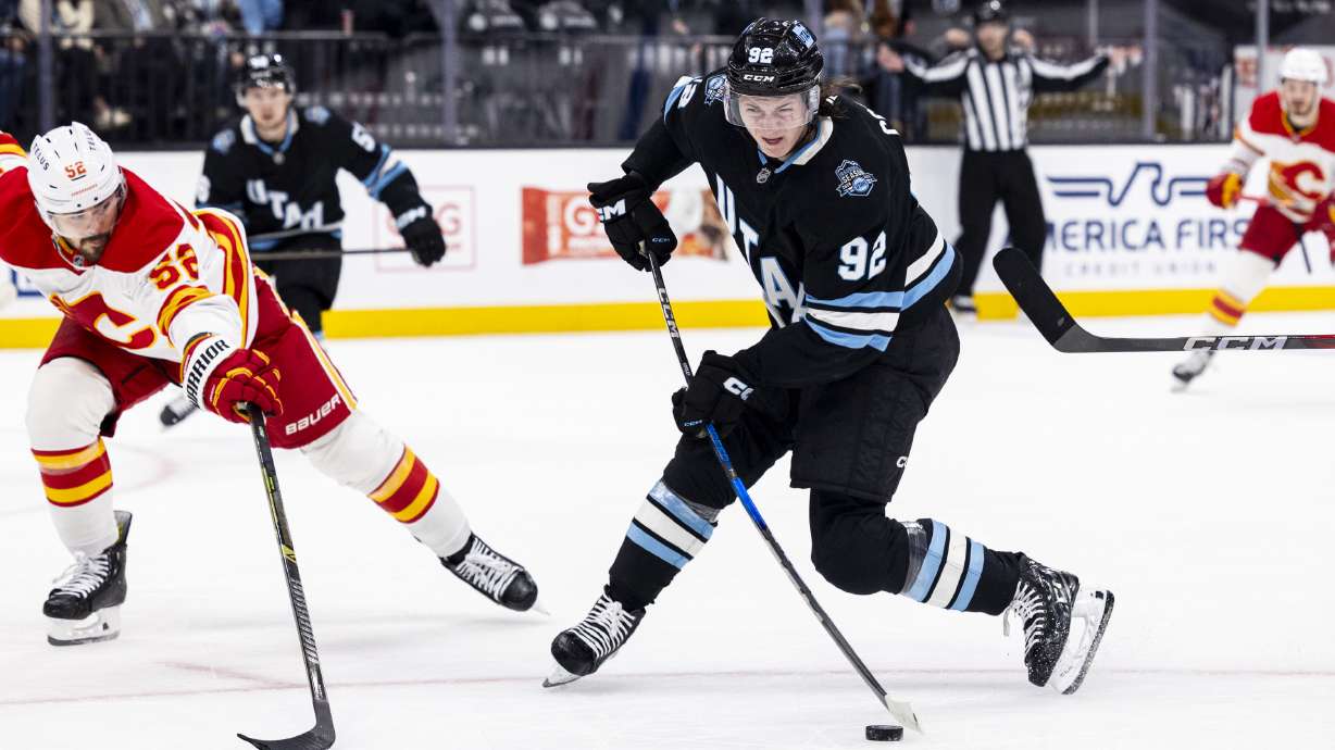 Utah Hockey Club center Logan Cooley (92) takes a shot on the goal while guarded by Calgary Flames defenseman MacKenzie Weegar (52) during an NHL game held at the Delta Center in Salt Lake City on Tuesday, April 1, 2025.