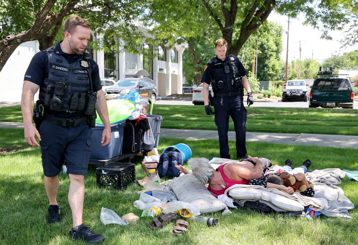Salt Lake Police Sgt. Ryan Sanders, who oversees the homeless resource center squad, and Salt Lake police officer Kent Krzymowski wake up two people to let them know they can’t camp on a park strip in Salt Lake City on Wednesday.