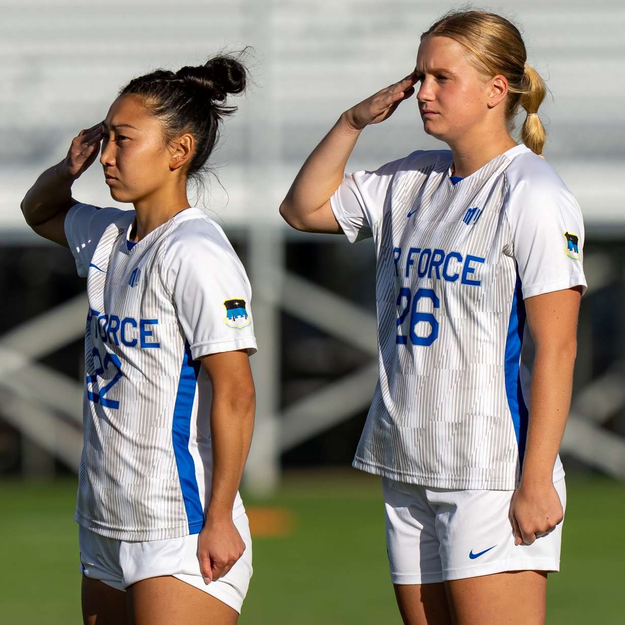 Caeli Sherman (right) and Raine Komata salute the flag during the national anthem. The Falcons will wear jerseys to honor the U.S. Space Force at least once this upcoming season.