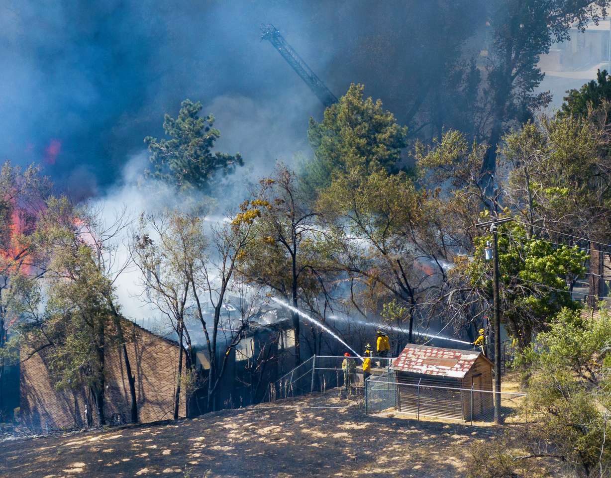 Firefighters work to douse the flames of a fire that started in a grassy area and then moved to nearby structures in Millcreek on Friday.
