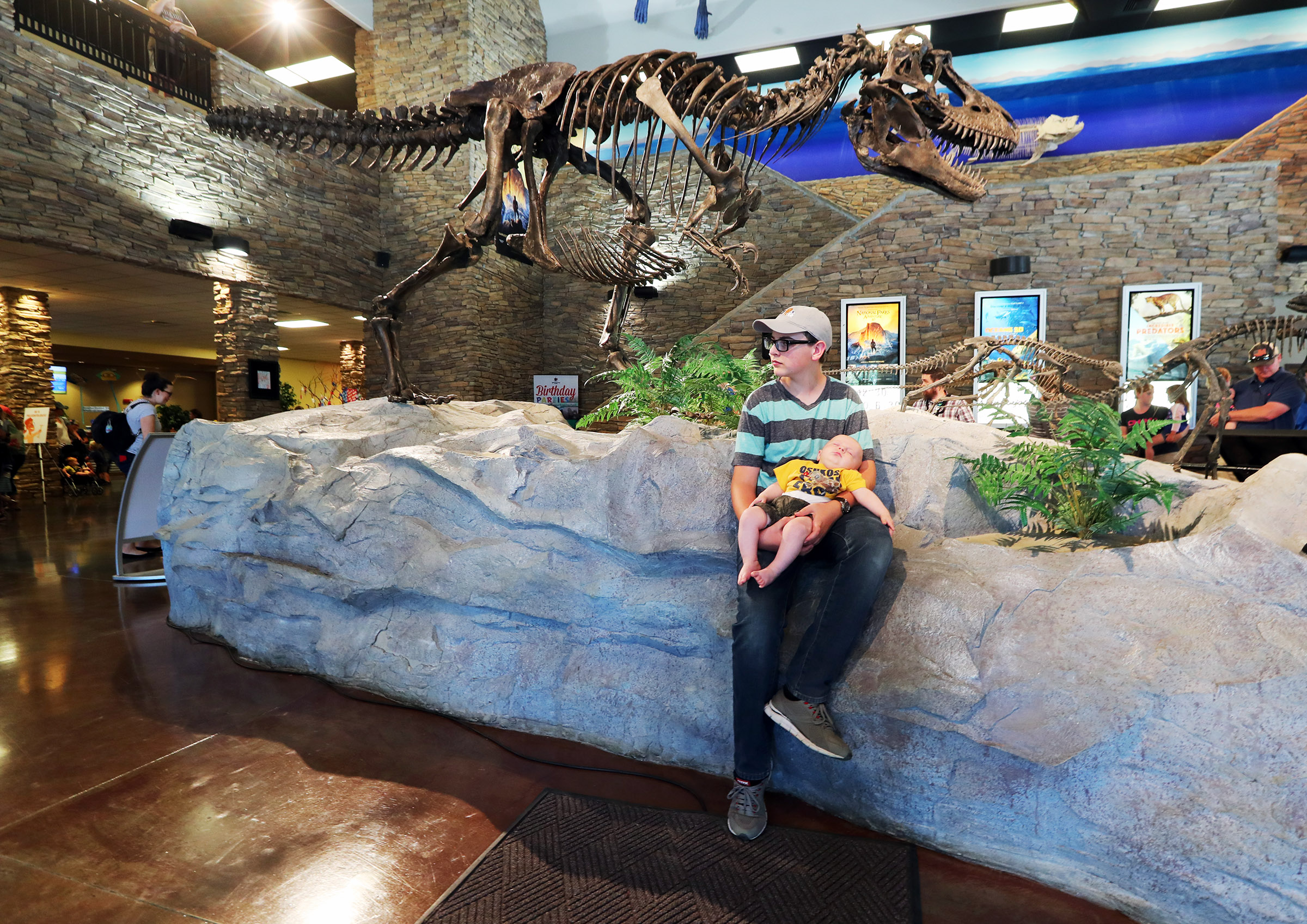 Evan Walker holds his baby brother, Isaac, near Ruth the Gorgosaurus at the Museum of Ancient Life at Thanksgiving Point in Lehi on June 22, 2018. The museum is one of the places you'll find family-friendly events this week.