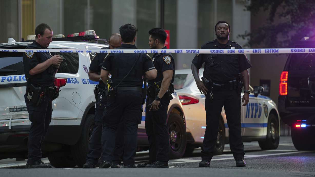 A New York Police officers gather at the scene on 52nd Street outside a Manhattan office building where two people were shot, including a New York police officer, Monday, July 28, 2025, in New York.