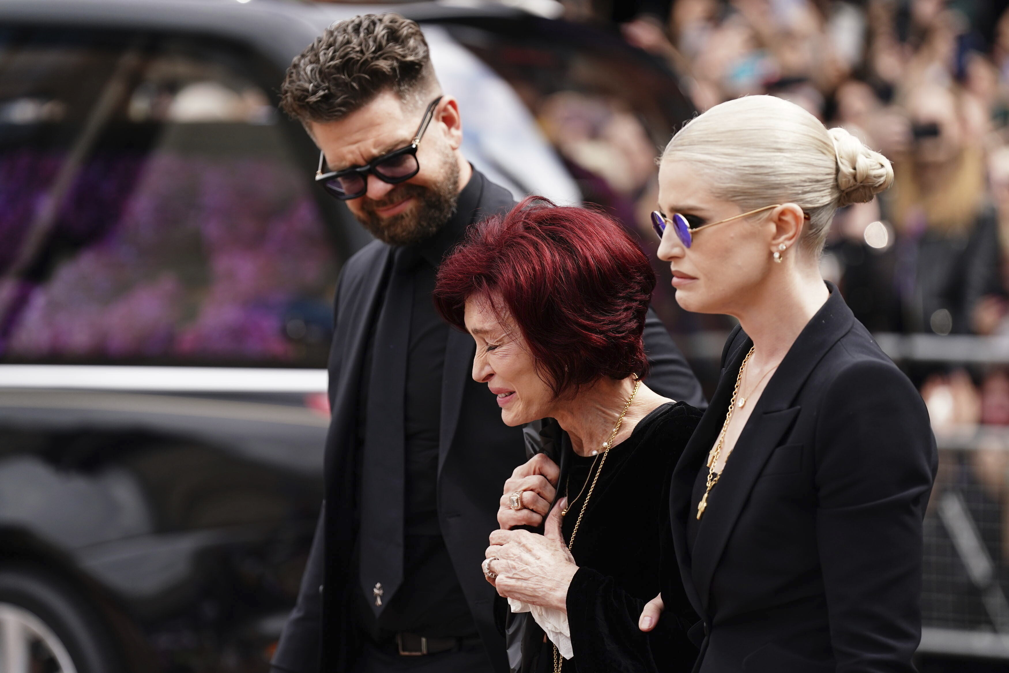 The family of Ozzy Osbourne from left, Jack Osbourne, Sharon Osbourne and Kelly Osbourne lay flowers and view the flowers left at the Black Sabbath Bridge bench on Broad Street in memory of Black Sabbath frontman Ozzy Osbourne ahead of the funeral procession, in Birmingham, England, Wednesday.