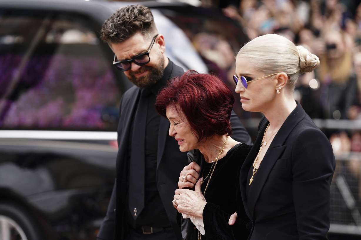 The family of Ozzy Osbourne from left, Jack Osbourne, Sharon Osbourne and Kelly Osbourne lay flowers and view the flowers left at the Black Sabbath Bridge bench on Broad Street in memory of Black Sabbath frontman Ozzy Osbourne ahead of the funeral procession, in Birmingham, England, Wednesday.